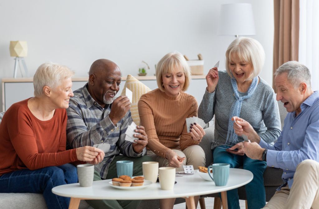 Seniors in assisted living socializing with one another playing cards and having snack in living room of senior community