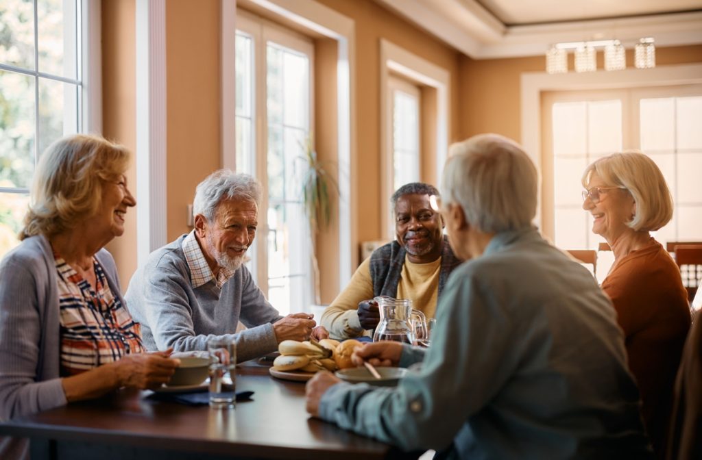A group of older adults chatting over a meal at a table in a retirement community.