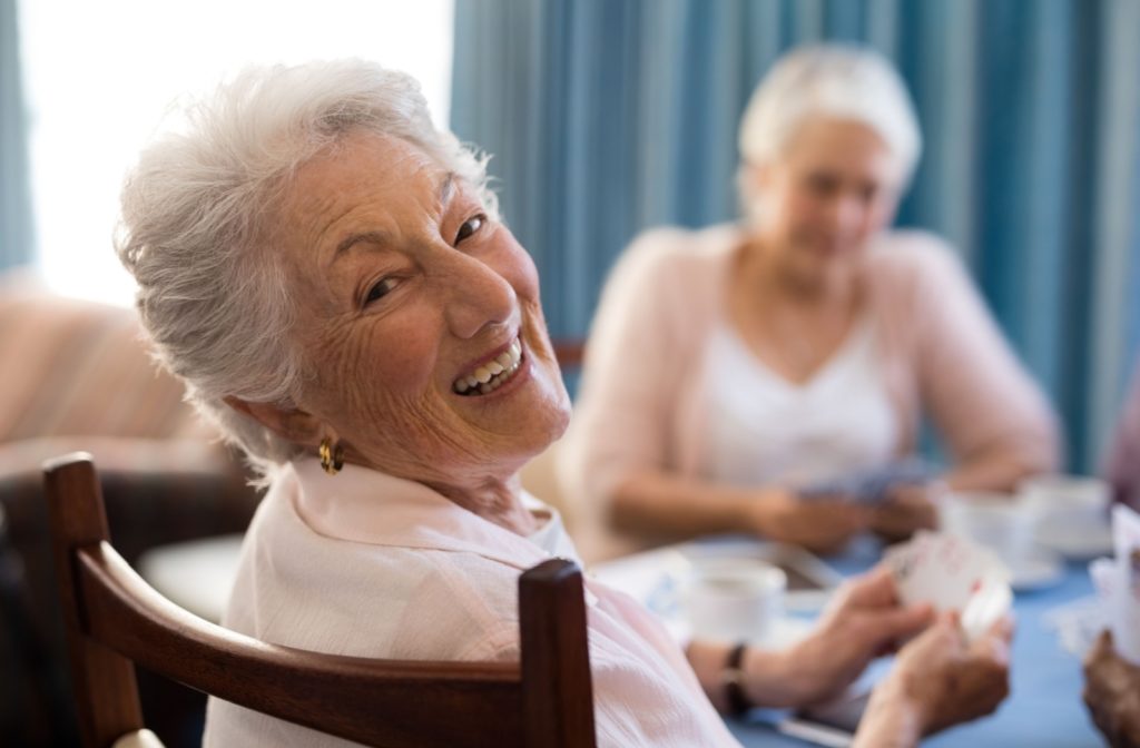 A group of older adults at a senior living community sit around a table laughing and playing cards together