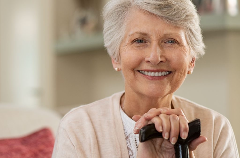 Close-up of a senior woman smiling and resting her hands on a cane