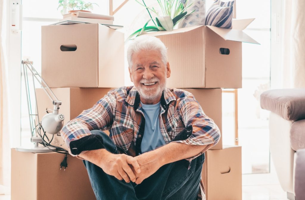 an older man is crouched down by his moving boxes as he transitions into his senior home.