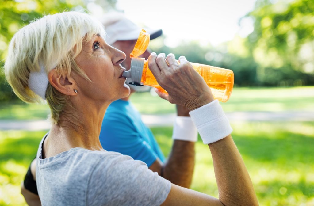 An older couple keeps hydrated by drinking from their waterbottles on a warm sunny day.